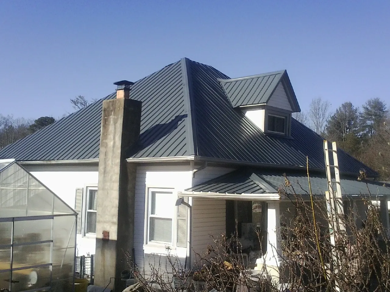 Dark blue standing seam metal roof on a white farmhouse with dormer — Slate & Tile Roof Repair by Roofing Brothers in Manson