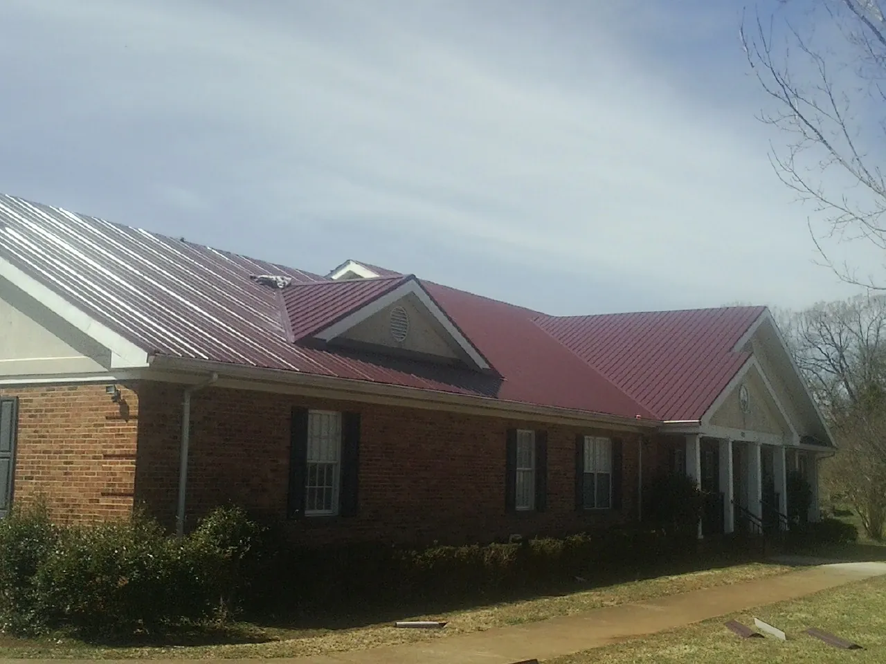 Red metal roof with gabled entries on a long brick building, from a Hail Damage Roof Repair job in Manson