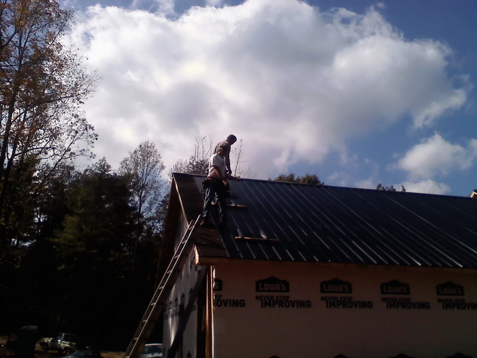 Roofer fastening dark metal panels high against a cloudy sky, from a Roof Inspection job in Manson