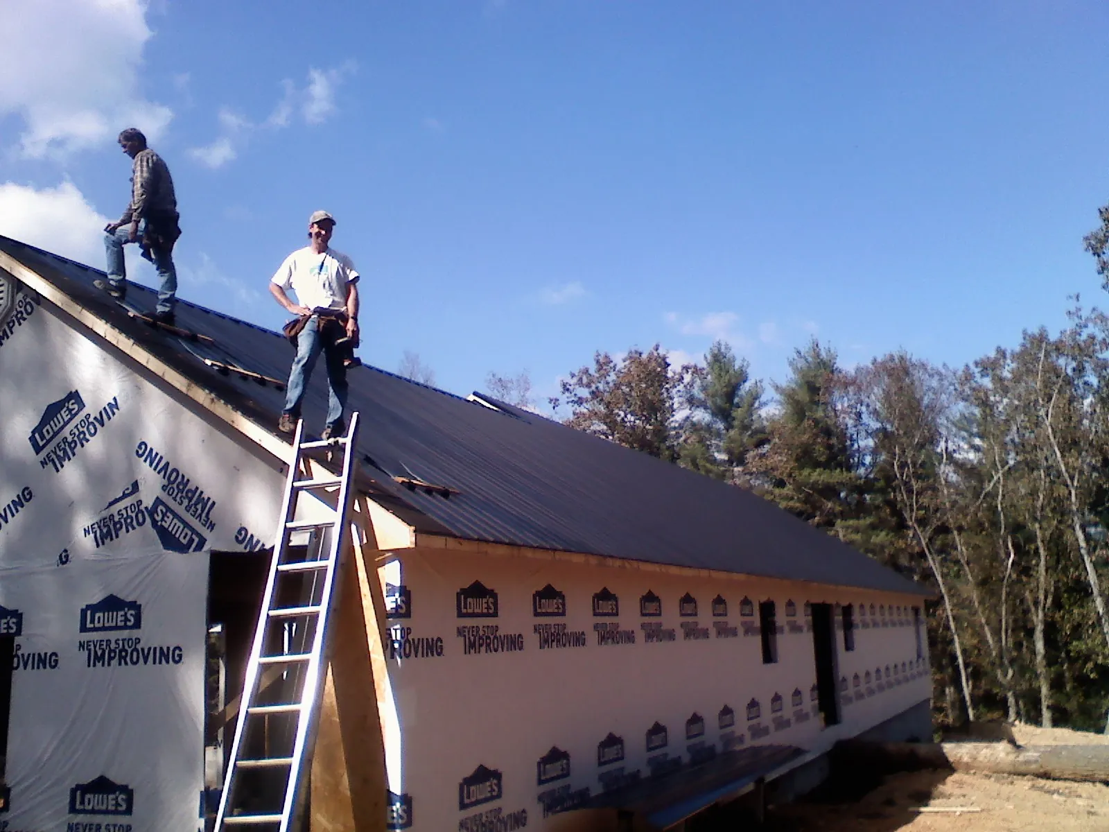 Two roofers standing on a long dark metal roof over a wrapped building in Manson