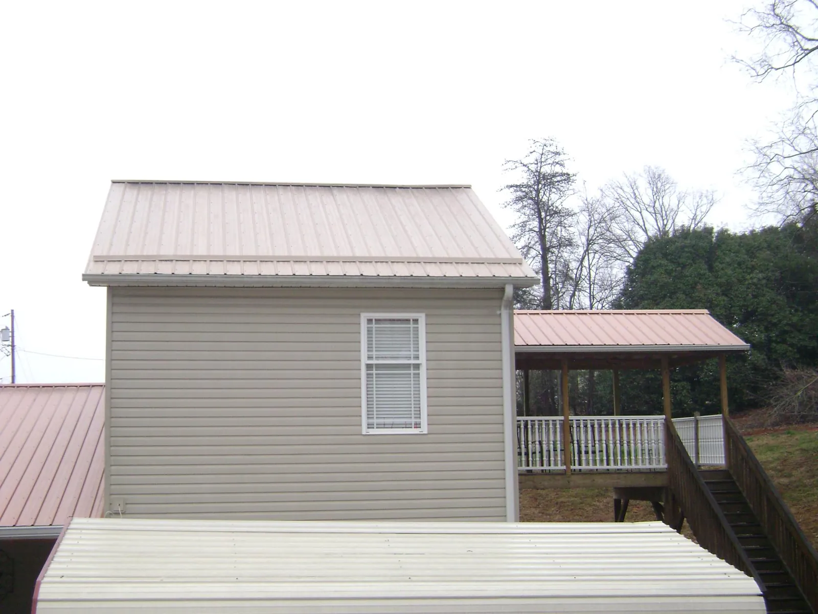 Tan metal roofs on a two story addition and attached porch, from a Roof Replacement job in Manson